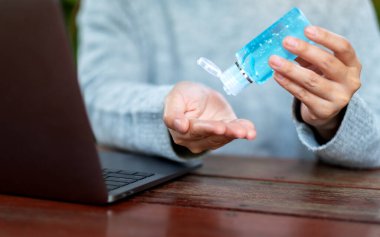 Sağlık ve Covid-19 veya 2020 virüs konsepti için evde dizüstü bilgisayar üzerinde çalışırken alkol jeli kullanan ve uygulayan bir kadının yakın plan görüntüsü