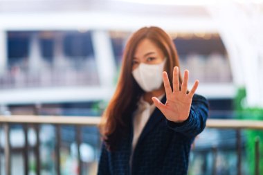 Korumacı yüz maskesi takan Asyalı bir kadının yakın plan görüntüsü Covid-19 'un yayılmasını önlemek için dur işareti yapıyor.  