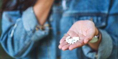 Beyaz ilaç kapsüllerini elinde tutan bir kadının yakın plan görüntüsü.