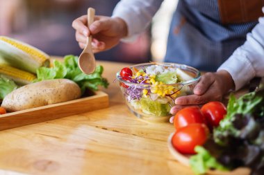 Mutfakta bir kase taze sebze salatası ve yemek pişiren bir kadın şefin yakın plan görüntüsü.