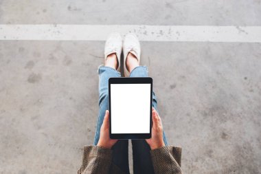 Üst görünümde, yerde otururken siyah tabletli beyaz ekranlı bir kadının görüntüsü var.