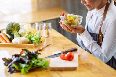 Mutfakta bir kase taze sebze salatası ve yemek pişiren bir kadın şefin yakın plan görüntüsü.
