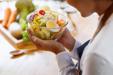 Mutfakta bir kase taze sebze salatası ve yemek pişiren bir kadın şefin yakın plan görüntüsü.
