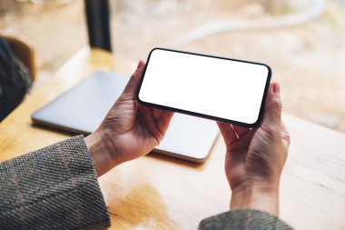 Masasında dizüstü bilgisayarı olan, boş beyaz masaüstü ekranlı cep telefonu tutan bir kadının görüntüsü. 