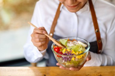 Güzel bir aşçının yemek pişirdiği ve mutfakta yenecek taze sebze salatası tuttuğu yakın plan görüntüsü.