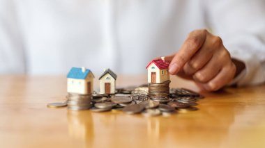 Para biriktirmek için ev modelini bozuk para yığınına koyan bir kadının yakın plan fotoğrafı.