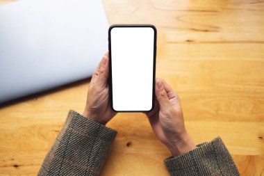 Masasında dizüstü bilgisayarı olan, boş beyaz masaüstü ekran cep telefonu tutan bir kadının en üstteki görüntüsü 