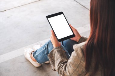 Yerde otururken elinde siyah tablet olan beyaz ekranlı bir kadının görüntüsü.