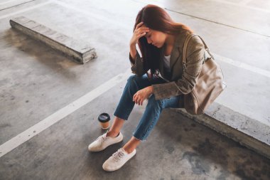 Stresli bir Asyalı kadın otoparkta tek başına oturuyor.