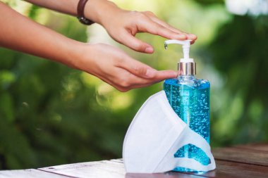 Sağlık ve Covid-19 ya da 2020 virüs konsepti için masadaki koruyucu maske ile elleri temizlemek için alkol jeli kullanan ve uygulayan bir kadının yakın plan görüntüsü