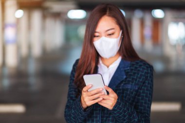 Hasta bir kadının koruyucu yüz maskesi taktığı, cep telefonunu sağlık ve Covid-19 konsepti için kullandığı yakın plan görüntüsü.