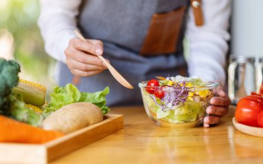 Mutfakta yemek pişiren ve elinde taze sebze salatası tutan bir kadın şefin yakın plan görüntüsü.