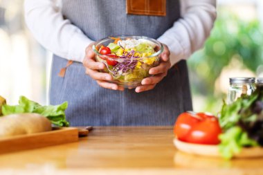 Mutfakta bir kase taze sebze salatası ve yemek pişiren bir kadın şefin yakın plan görüntüsü.