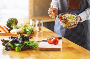 Mutfakta yemek pişiren ve elinde taze sebze salatası tutan bir kadın şefin yakın plan görüntüsü.