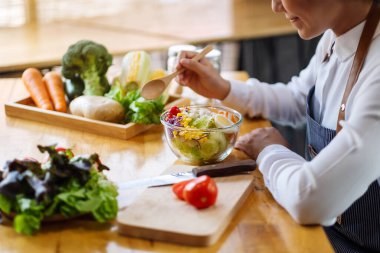 Mutfakta yemek pişiren ve elinde taze sebze salatası tutan bir kadın şefin yakın plan görüntüsü.