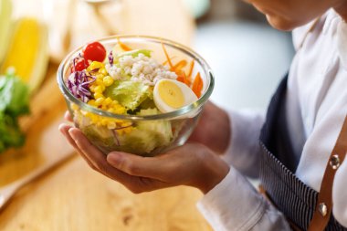 Mutfakta bir kase taze sebze salatası ve yemek pişiren bir kadın şefin yakın plan görüntüsü.