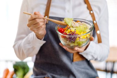 Mutfakta yemek pişiren ve elinde taze sebze salatası tutan bir kadın şefin yakın plan görüntüsü.