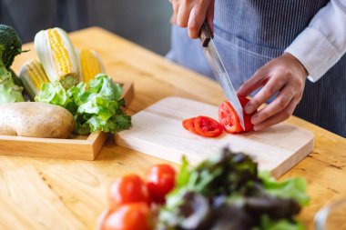 Tahtada bıçakla domates doğrayan bir kadın şefin yakın plan görüntüsü.