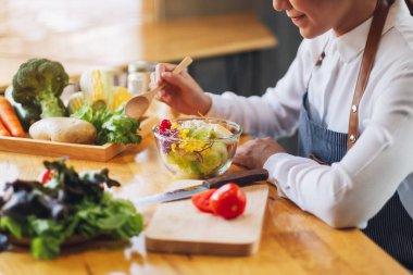 Closeup image of a female chef cooking and eating a bowl of fresh mixed vegetables salad in kitchen