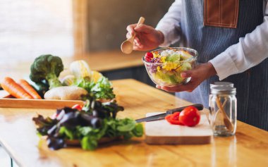 Mutfakta yemek pişiren ve elinde taze sebze salatası tutan bir kadın şefin yakın plan görüntüsü.