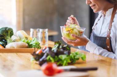 Güzel bir aşçının yemek pişirdiği ve mutfakta yenecek taze sebze salatası tuttuğu yakın plan görüntüsü.