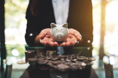 Closeup image of a businesswoman holding piggy bank with pile of coins on the table for saving money and financial concept