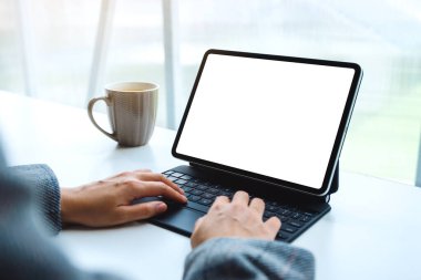 Tablet klavyesinde bilgisayar bilgisayarı olarak beyaz masaüstü ekranı ve masada kahve fincanını kullanan ve yazan ellerin görüntüsü