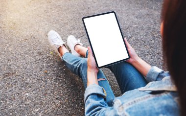 Üst görünümde, açık havada otururken elinde siyah bir tablet olan beyaz ekranlı bir kadının görüntüsü var.