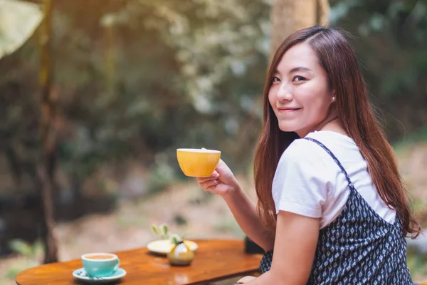 Açık havada elinde sıcak kahve tutan ve içen Asyalı güzel bir kadının yakın çekimi.