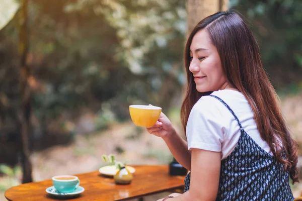 Açık havada elinde sıcak kahve tutan ve içen Asyalı güzel bir kadının yakın çekimi.