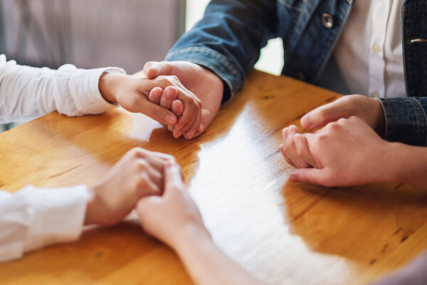 Group of people sitting in a circle holding hands and pray together or in therapy session 