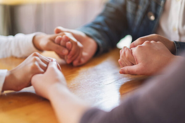 Group of people sitting in a circle holding hands and pray together or in therapy session 