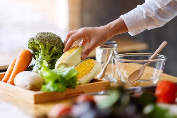 Sebze tepsisinden taze mısır toplayan bir kadın şef.