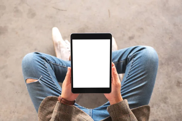 Üst görünümde, yerde otururken siyah tabletli beyaz ekranlı bir kadının görüntüsü var.