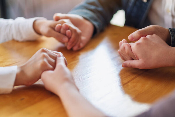 Group of people sitting in a circle holding hands and pray together or in therapy session 