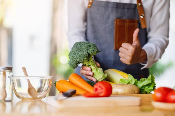 Masada sebze tepsisi olan yeşil brokoliye iyi bir işaret göstermek için baş parmak kaldıran bir kadın şef.