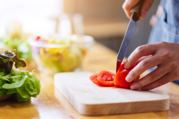 Closeup image of a woman chef cutting and chopping tomato by knife on wooden board