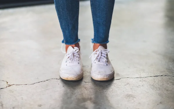 一名妇女穿着牛仔和白色运动鞋站在水泥地板上的照片 — 图库照片