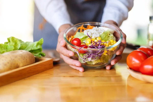 Mutfakta bir kase taze sebze salatası ve yemek pişiren bir kadın şefin yakın plan görüntüsü.