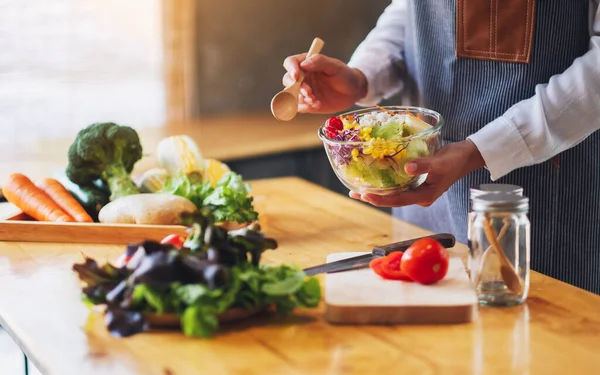 Mutfakta yemek pişiren ve elinde taze sebze salatası tutan bir kadın şefin yakın plan görüntüsü.