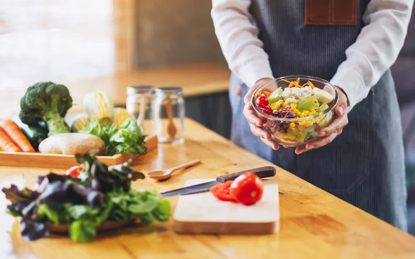 Mutfakta bir kase taze sebze salatası ve yemek pişiren bir kadın şefin yakın plan görüntüsü.