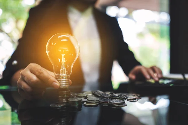 コインの上に電球を置くビジネスマンは 省エネルギーとお金の概念を計算しながら テーブルの上に積層 — ストック写真