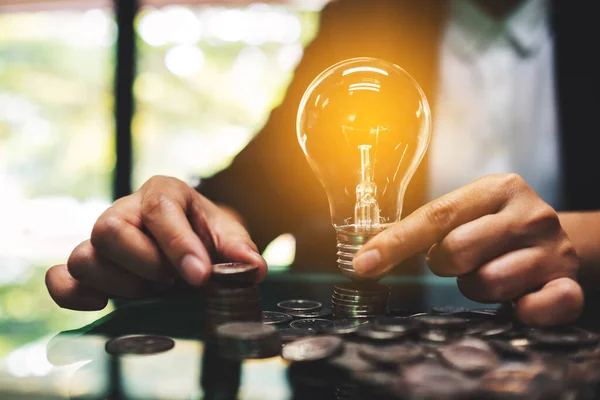 Empresaria Sosteniendo Bombilla Mientras Apila Monedas Mesa Para Ahorrar Energía —  Fotos de Stock