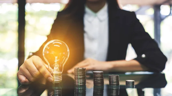 Businesswoman Holding Lightbulb Next Coins Stack Table Saving Energy Money — Fotografia de Stock