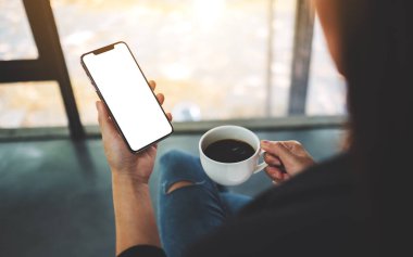 Kahve içerken elinde boş ekranla cep telefonu tutan bir kadının görüntüsü. 