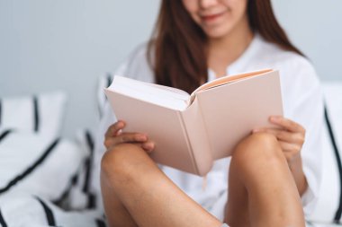 Evdeki rahat bir yatakta kitap okuyan güzel bir kadının yakın plan görüntüsü.