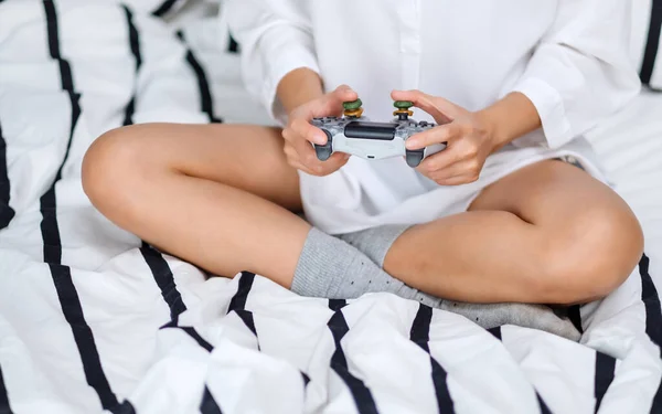ゲーム中にゲームコントローラーを持っている女性のクローズアップイメージ 自宅で白い居心地の良いベッドの上に座って — ストック写真