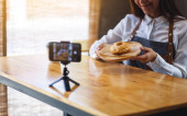 A beautiful asian woman food blogger or vlogger showing a piece of donut while recording a video on camera 