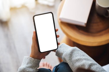 Üst görünümde, evde yatak odasında otururken elinde boş masaüstü ekran olan cep telefonu tutan bir kadının görüntüsü