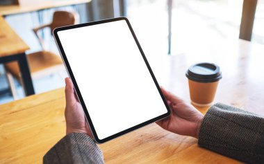 Siyah tabletli, beyaz ekranlı ve ahşap masada kahve fincanı olan bir kadının görüntüsü.